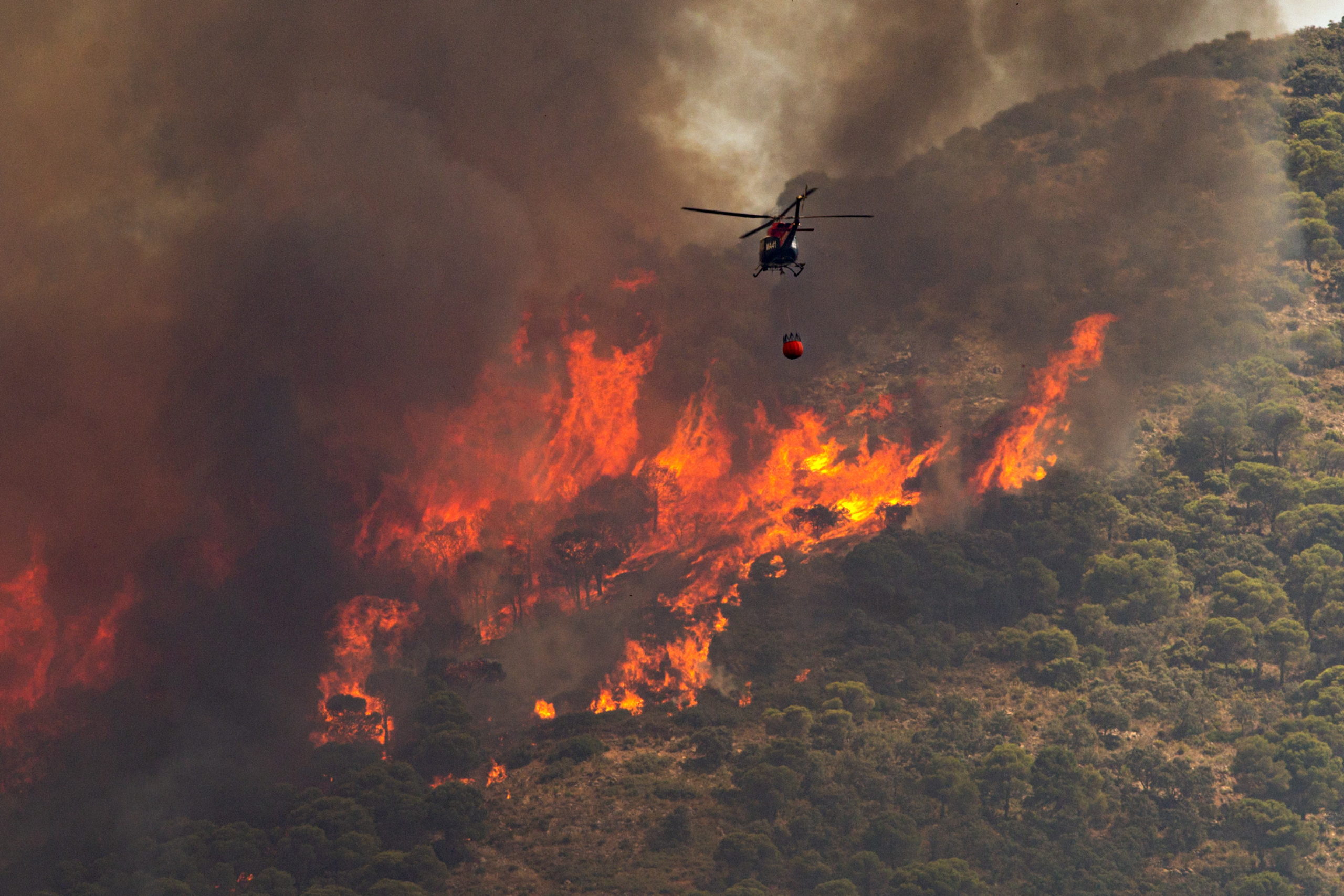 epa10072820 A helicopter pours water into the flames of a forest fire in Mijas, Malaga, southern Spain, 15 July 2022. Regional authorities activated the first level of the Emergency Plan for Forest Fire Emergencies as the fire has been spreading since noon and some residential areas have already been evacuated.  EPA-EFE/DANIEL PEREZ